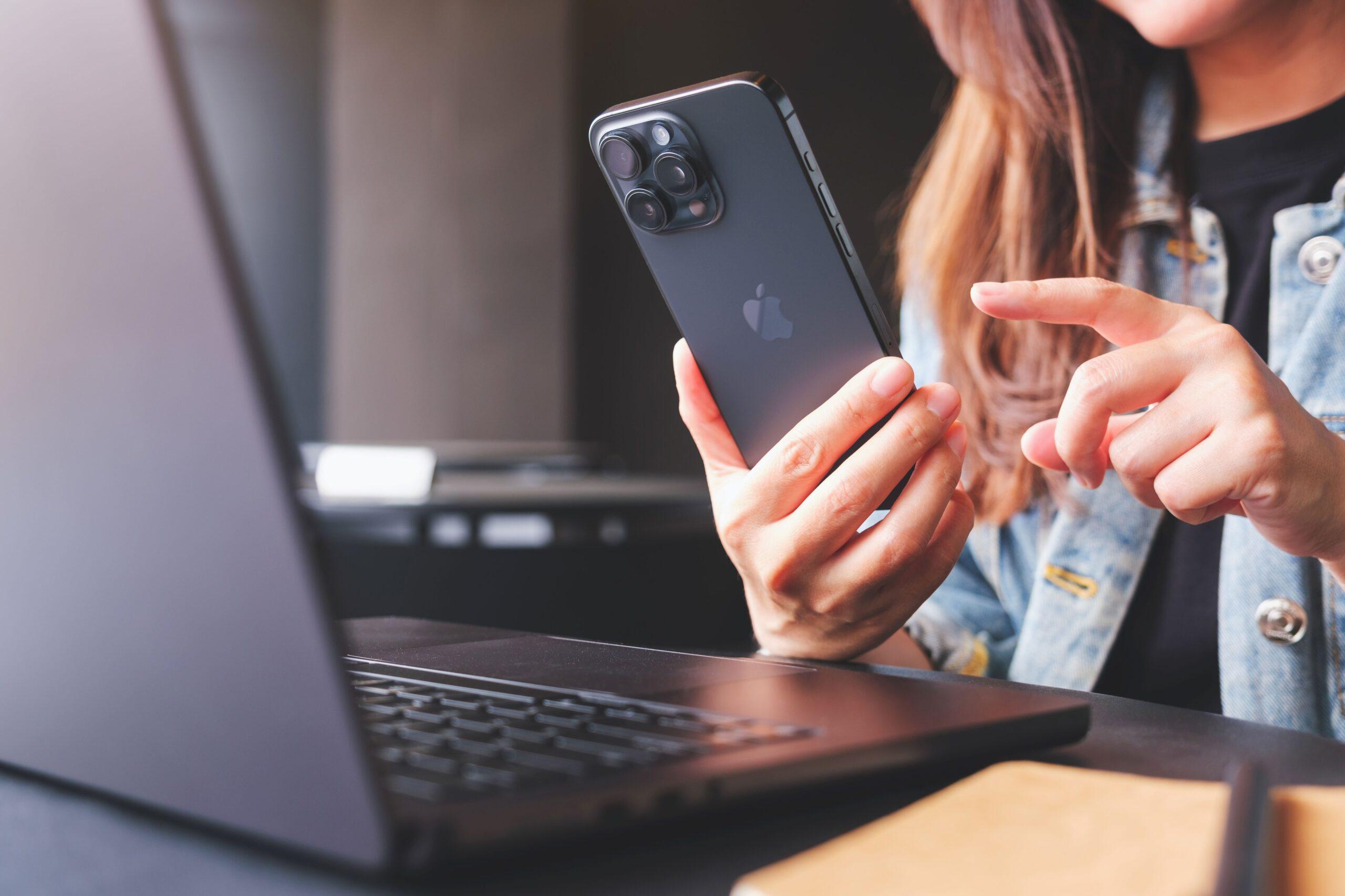 Eine Frau mit Iphone sitzt vor einem Laptop