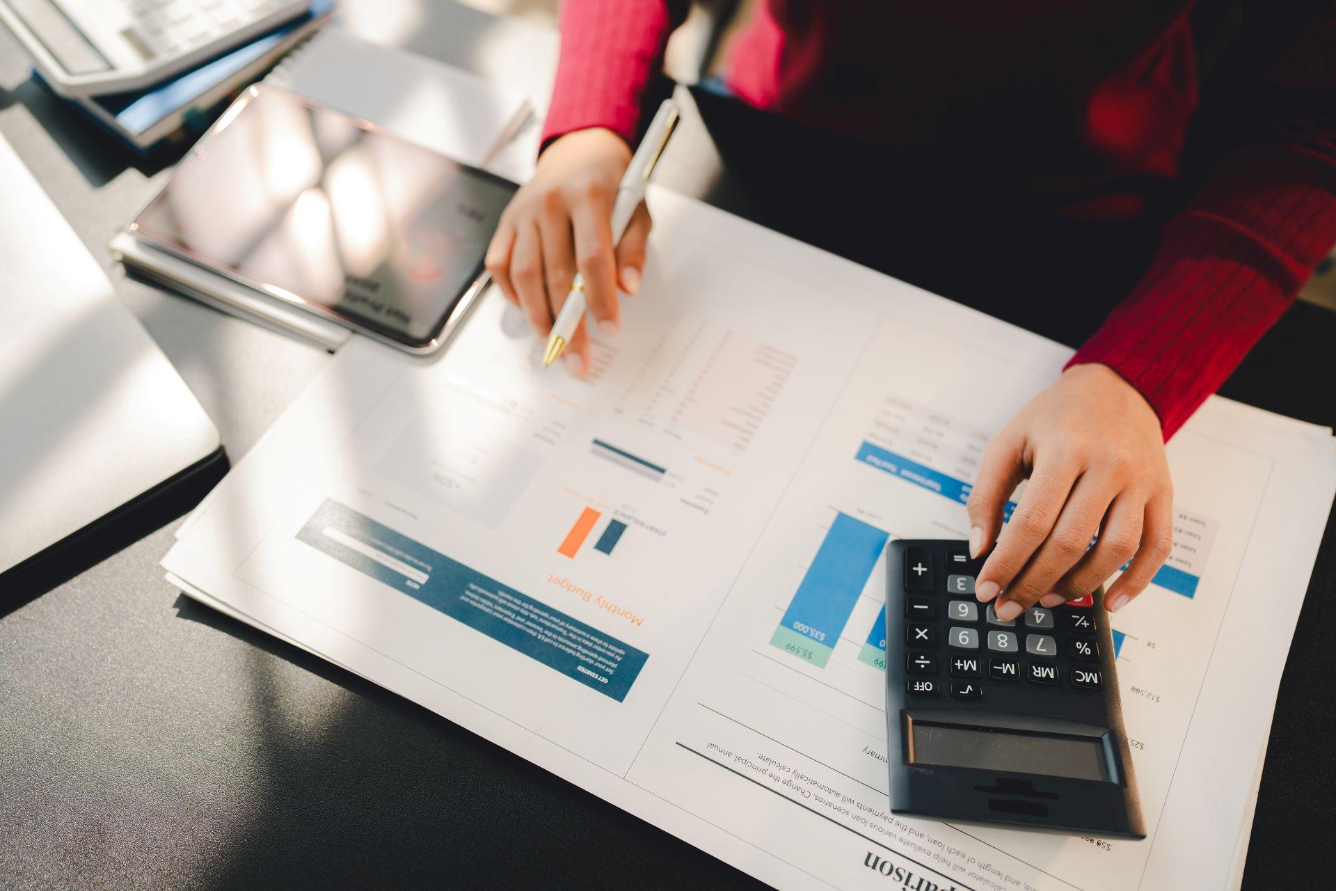 Person analysiert Finanzdokumente mit Taschenrechner und Tablet und steht stellvertretend fuer digitale und praezise Steuerberatung in Neu-Ulm